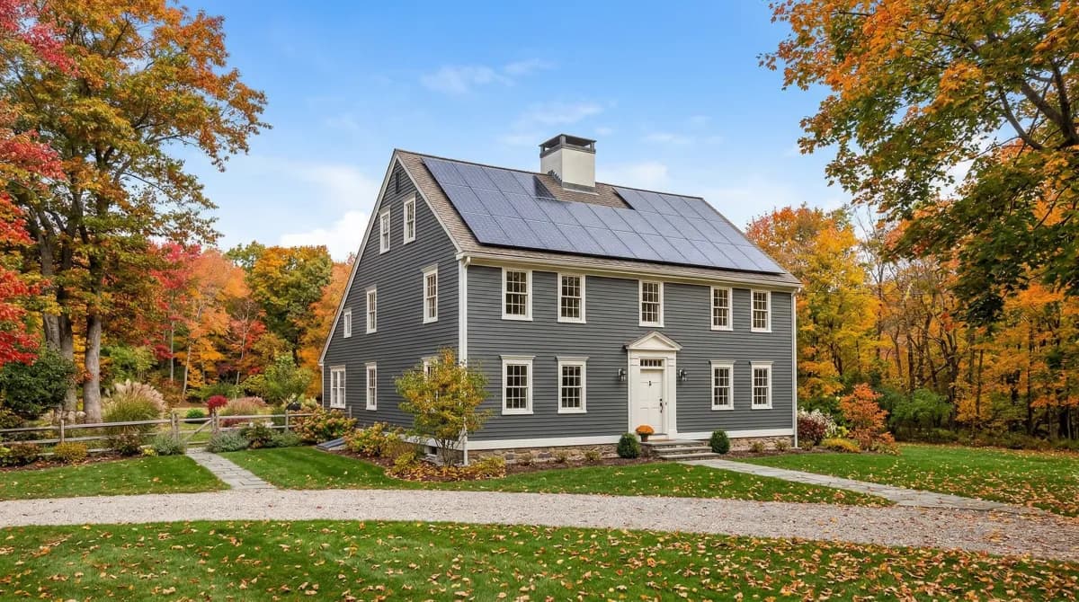Connecticut colonial home with rooftop solar panels surrounded by autumn foliage under blue sky